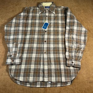 May include: A long-sleeved, button-down shirt with a plaid pattern in shades of grey, brown, and white. The shirt has a collar, a chest pocket, and buttoned cuffs. A tag is attached to the shirt.