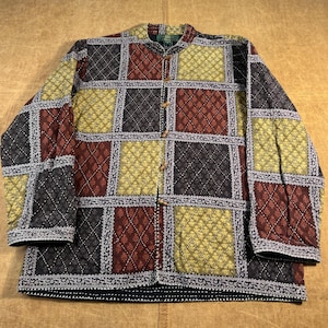 May include: A quilted jacket with a patchwork design. The jacket features a mandarin collar and wooden buttons. The squares are in shades of black, burgundy, yellow, and olive green, with a decorative border. The jacket is laid flat on a light brown surface.