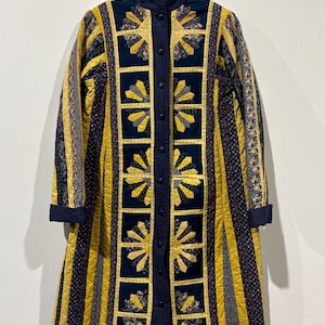 May include: A long, quilted coat with a navy blue collar and button closure. The coat features a striking design with yellow fan-shaped patterns on a navy blue background, and vertical yellow and navy blue stripes. The sleeves have navy blue cuffs.