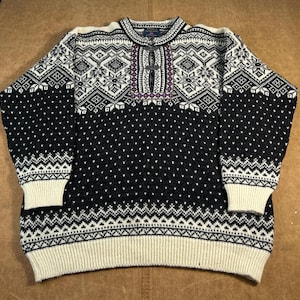 May include: A black and white patterned jumper with a round neckline and long sleeves. The jumper features a geometric design on the upper chest and sleeves, with a dotted pattern on the lower half. The cuffs and hem are cream-coloured.