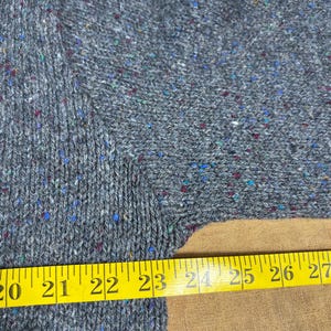 May include: Close-up of a gray knit sweater with flecks of blue, red, and green. A yellow measuring tape shows a length of 20 to 27 inches. The sweater has a textured appearance.