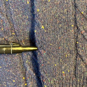 May include: Close-up of a navy blue knit fabric with flecks of yellow, red, and green. The fabric has a textured appearance and is likely from a sweater or other garment. A black pen is partially visible.