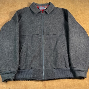 Peut inclure: Veste en laine grise avec fermeture éclair intégrale, col et deux poches avant. La veste a un ourlet et des poignets côtelés. L'intérieur du col est doublé d'un motif à carreaux rouge et noir.