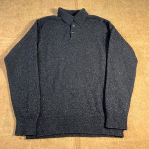 May include: A charcoal gray sweater with a collared neckline and two buttons. The long-sleeved sweater has ribbed cuffs and a ribbed hem. The fabric has a textured appearance.