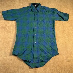 Peut inclure: Chemise à manches courtes à carreaux bleus et verts. Elle présente une fermeture boutonnée, un col et une poche poitrine unique. Le tissu semble être léger et confortable.