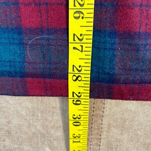 May include: A yellow measuring tape shows measurements from 66 to 84 cm. The tape is next to a red and teal plaid fabric. The fabric is on a tan surface.
