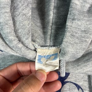 May include: Close-up of a gray hooded sweatshirt with a navy blue Mickey Mouse graphic. The tag reads "Disney Casuals" and "Large". The sweatshirt is made of a soft, textured fabric.