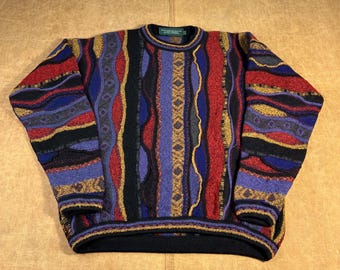 May include: A colorful, patterned sweater with a crew neck. The sweater features vertical stripes in red, blue, black, purple, and gold. The cuffs and hem are black. The sweater is made of a thick, textured material.