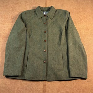 May include: A long-sleeved olive green jacket featuring a classic collar, a full-length front button closure with six brown buttons, and two vertical side pockets. The garment is constructed from a textured fabric and includes a visible brand label.