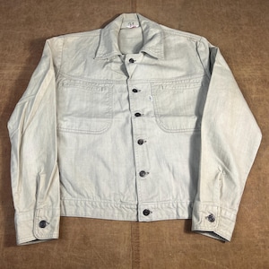 May include: A light beige denim jacket with a button-up front, two chest pockets, and two side pockets. The jacket has a classic collar and buttoned cuffs. The jacket is a light color and appears to be vintage.