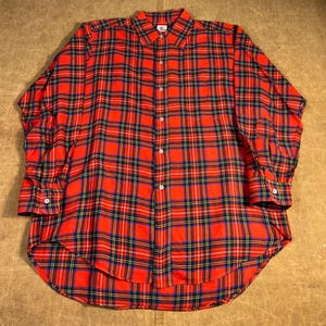 May include: A red tartan check shirt with long sleeves. The shirt has a button-down collar and cuffs. The plaid pattern includes navy blue, yellow, and green lines. The fabric appears to be a medium-weight woven material. The shirt is a classic style.