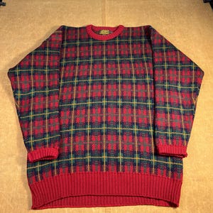 May include: A red, green, and navy blue plaid sweater with a ribbed red collar, cuffs, and hem. The sweater has a crew neck and a classic, comfortable fit. The plaid pattern is a traditional design.