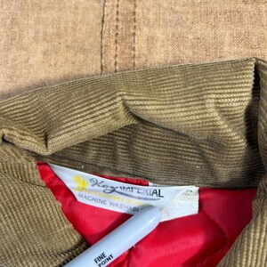 May include: Close-up of a tan corduroy jacket collar with a red quilted lining. The jacket's label reads "Key Imperial" and "Machine Washable". A silver Sharpie pen is in the foreground.