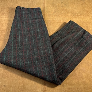 May include: Dark gray plaid trousers with a red and teal grid pattern. The pants are folded and laid flat, showcasing the fabric's texture and design. The trousers have a button closure and a back pocket.