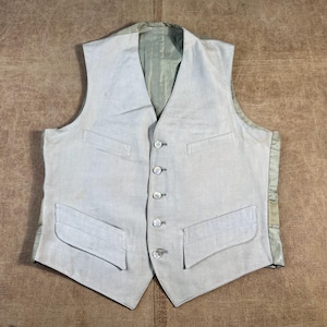 May include: A light gray vest with four buttons down the front and two front pockets. The vest has a light green lining and is made of a textured fabric. The vest is a classic style.