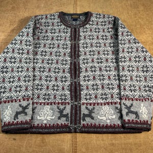 May include: A gray, white, and burgundy wool cardigan sweater with a snowflake and reindeer pattern. The sweater has a round neck, long sleeves, and decorative metal clasps down the front. The bottom hem features a band with reindeer and tree designs.