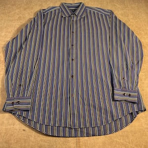 May include: A long-sleeved button-down shirt with vertical stripes in blue, yellow, white, and brown. The shirt has a classic collar and buttoned cuffs. The fabric appears to be woven, with a subtle texture. The shirt is laid flat on a neutral surface.