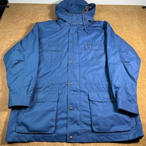 May include: A blue hooded jacket with multiple pockets and a drawstring. The jacket has a button-up front and a D-ring detail on the chest. The jacket is made of a durable material and is suitable for outdoor activities.