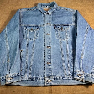 May include: A light blue denim jacket with a button-up front, two chest pockets, and two side pockets. The jacket has a classic collar and buttoned cuffs. The denim has a faded appearance, and the jacket is likely a vintage or pre-owned item.