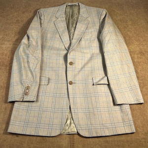 May include: A light beige blazer with a plaid pattern in light blue and beige. The blazer has a notched lapel, two front pockets, and three buttons on each cuff. The jacket is made of a woven fabric.