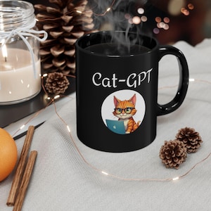 Pode incluir: Caneca de cerâmica preta com o texto "Cat-GPT" e uma ilustração de desenho animado de um gato laranja usando óculos e um laptop. A caneca tem uma alça curva e é preenchida com um líquido escuro, possivelmente café ou chá.