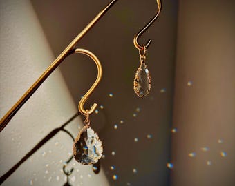 May include: A pair of gold teardrop earrings with clear crystal stones hanging from a gold stand.