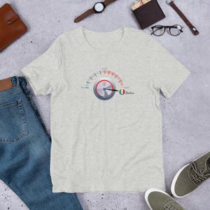 May include: Light gray t-shirt featuring a graphic of a speedometer with the Italian flag and the word "Italian". The speedometer needle points to the right. The shirt is made of a soft material.