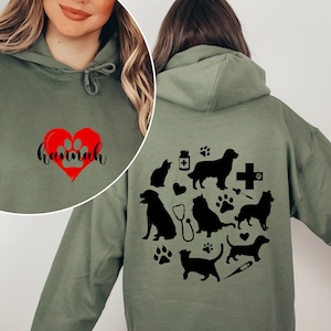 May include: A military green hooded sweatshirt with a black paw print heart and the name "Hannah" on the front. The back of the sweatshirt features a black silhouette design of various animals, including dogs, cats, and a stethoscope.