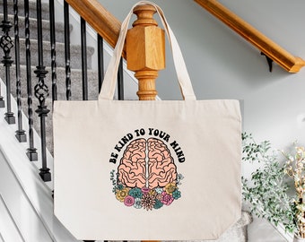 May include: A natural canvas tote bag with a pink brain illustration and the text "Be Kind to Your Mind". The brain is surrounded by colorful flowers.