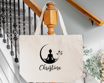May include: A natural canvas tote bag with a black silhouette of a person meditating in a crescent moon with a lotus flower. The text "Christina" is printed below the image.