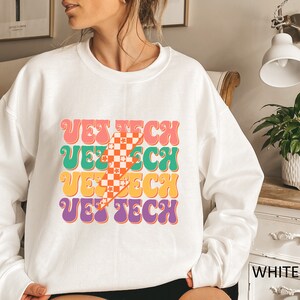 May include: White sweatshirt with a retro-style graphic that says "VET TECH" in colorful, layered letters. The graphic features a checkered pattern and a lightning bolt.