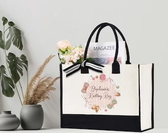 May include: A white canvas tote bag with black handles and a black bottom. The bag has a pink and white knitted design with the text "Stephanie's Knitting Bag" in brown lettering. The bag is decorated with watercolor illustrations of knitting needles, yarn, and other knitting supplies.