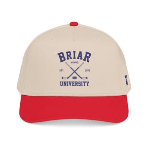 May include: A baseball cap with a cream-colored crown and a red brim. The cap features the text "Briar Hawks University" in navy blue, along with crossed hockey sticks and a hockey puck.