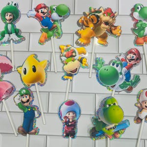以下が含まれることがあります： マリオ、ルイージ、ピーチ姫、ヨッシー、クッパ、クッパJr.、キノピオ、黄色いルマなど、スーパーマリオのキャラクターが描かれた12個のデコレーション用ケーキトッパー。各カットアウトにはホログラムの縁取りと白いスティックが付いています。