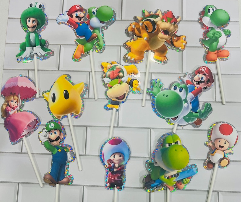 以下が含まれることがあります： マリオ、ルイージ、ピーチ姫、ヨッシー、クッパ、クッパJr.、キノピオ、黄色いルマなど、スーパーマリオのキャラクターが描かれた12個のデコレーション用ケーキトッパー。各カットアウトにはホログラムの縁取りと白いスティックが付いています。
