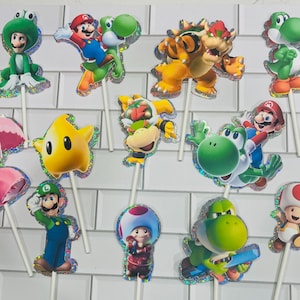 以下が含まれることがあります： マリオ、ルイージ、ピーチ姫、ヨッシー、クッパ、クッパJr.、キノピオ、黄色いルマなど、様々なスーパーマリオのキャラクターが描かれた12個のデコレーション用ケーキトッパー。それぞれホログラムの縁取りが施され、白いスティックに取り付けられています。