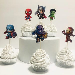 May include: Six white cupcakes with different superhero character toppers. The toppers include Spiderman, Thor, Hulk, Captain America, Thanos, and Iron Man.