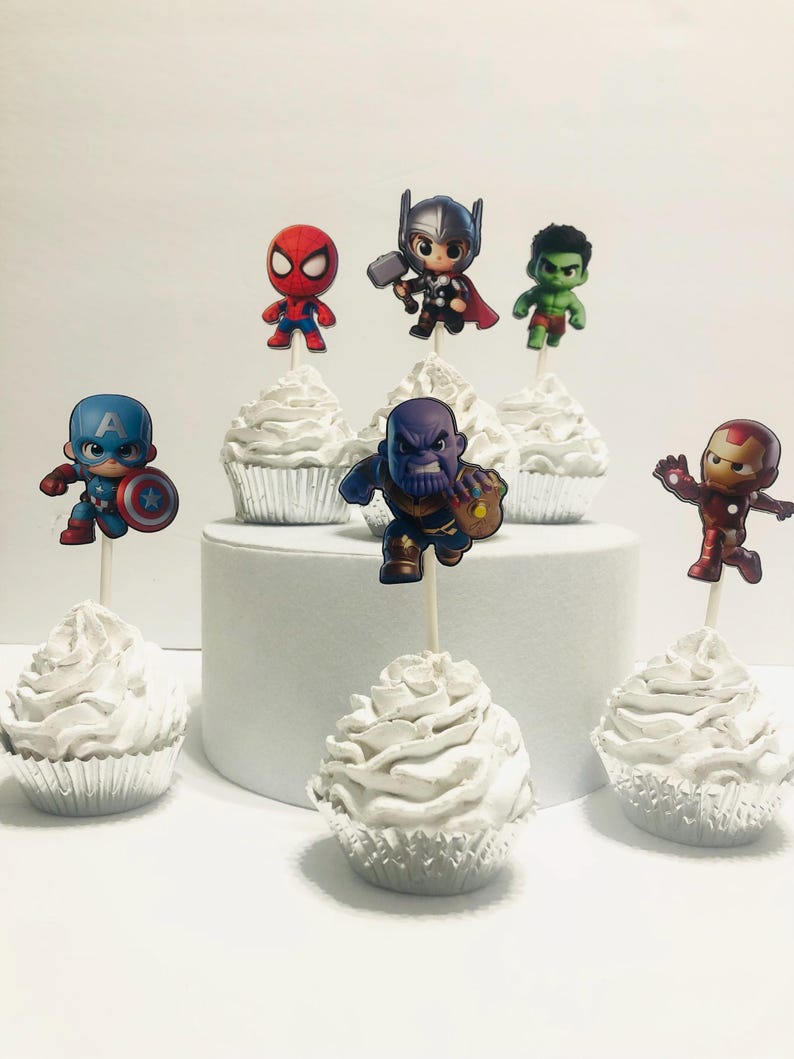 May include: Six white cupcakes with different superhero character toppers. The toppers include Spiderman, Thor, Hulk, Captain America, Thanos, and Iron Man.