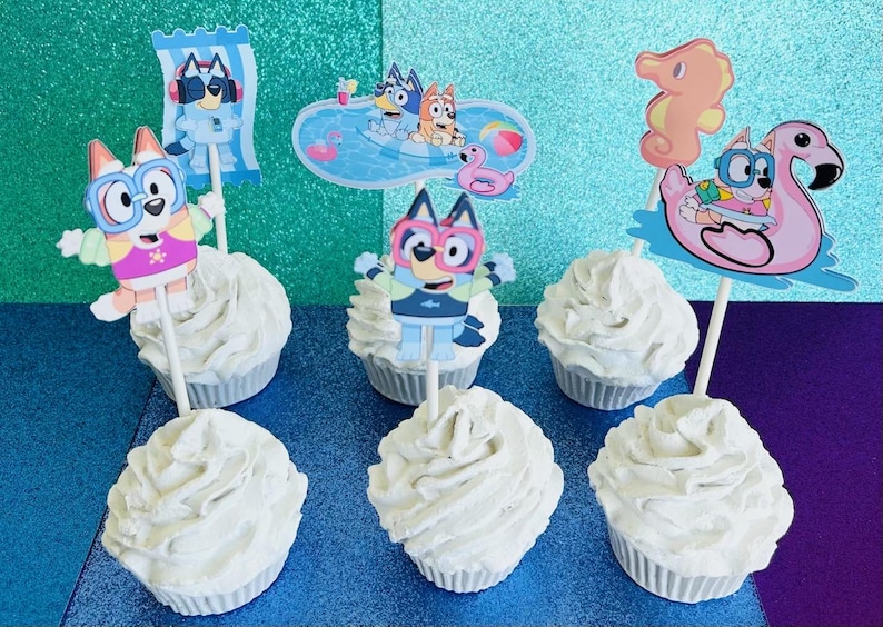 May include: Six cupcakes with white frosting, each topped with a character from the animated series Bluey. The toppers feature Bluey and Bingo in swimwear, sunglasses, and pool floats. The background is a sparkly teal and purple.