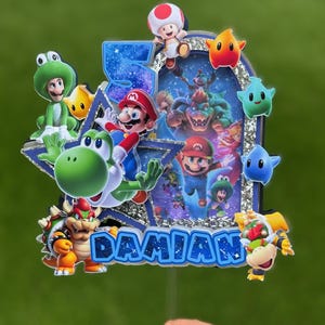 K&ouml;nnte beinhalten: Ein mehrschichtiger Tortenaufleger mit dem Namen DAMIAN und der Zahl 5. Das Design zeigt verschiedene Super Mario-Figuren wie Mario, Yoshi, Bowser und Toad vor einem glitzernden blau-silbernen Hintergrund mit Sternenmotiven.
