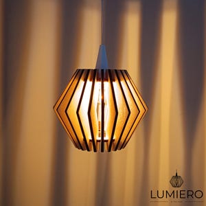 May include: A geometric wooden pendant light fixture with a warm, inviting glow. The light has a white top and a diamond-shaped shade made of wooden slats. The light fixture is suspended from a white cord.