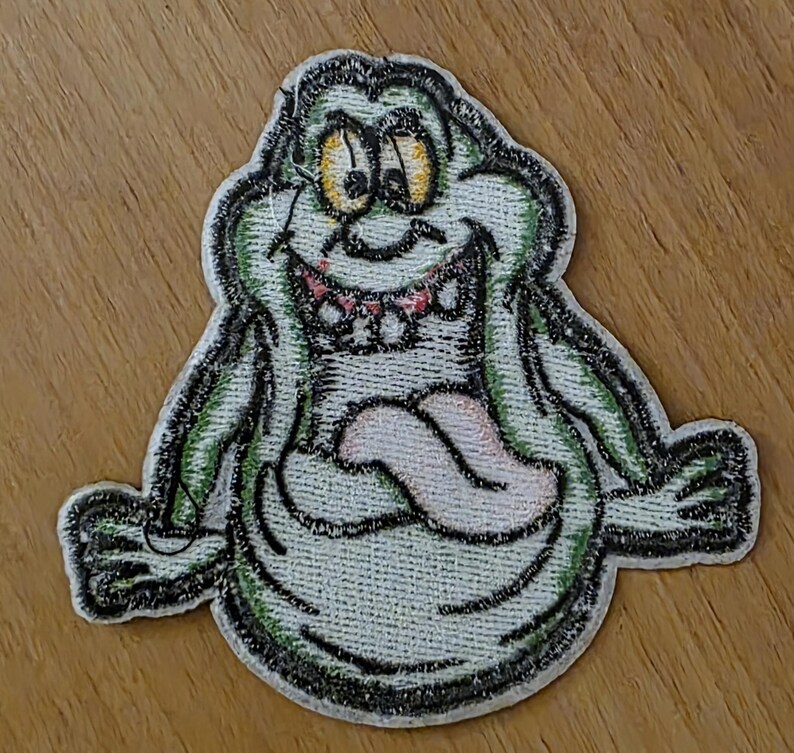 Puede incluir: Parche bordado con un personaje de fantasma de dibujos animados con una amplia sonrisa y una larga lengua. El parche tiene un cuerpo verde claro, contorno negro y ojos amarillos. La lengua es rosa y los dientes son rojos. Para ropa o accesorios.