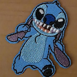 Puede incluir: Parche bordado con el personaje Stitch de Lilo & Stitch. El parche es principalmente azul con detalles en negro, morado y rosa. Stitch está sonriendo, con grandes ojos negros y una boca detallada. El parche está diseñado para planchar.