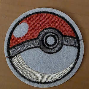 Könnte beinhalten: Gestickter Aufnäher mit einem rot-weißen Pokeball-Design. Der Aufnäher hat einen hellblauen Hintergrund mit detaillierten silbernen, schwarzen und roten Nähten. Der kreisförmige Aufnäher ist ein beliebtes Produkt für Fans der Pokémon-Franchise.