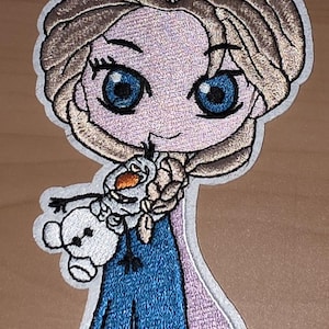 Könnte beinhalten: Gestickter Aufnäher mit einer Cartoon-Darstellung einer Figur mit blonden Haaren, blauen Augen und einem blauen Kleid, die einen kleinen Schneemann hält. Der Aufnäher hat einen weißen Rand und ist für Kleidung oder Accessoires geeignet.