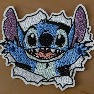 Könnte beinhalten: Gestickter Aufnäher mit der Figur Stitch aus Lilo & Stitch. Stitch wird dargestellt, wie er durch einen zerrissenen Hintergrund bricht. Der Aufnäher zeigt Stitchs blauen Körper, große Augen, lila Ohren und ein breites Grinsen. Er hat einen weißen Rand.