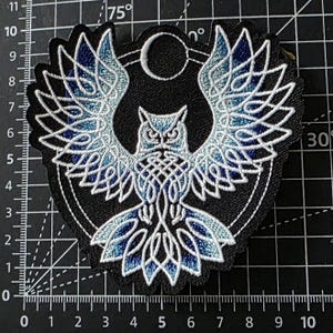 May include: Embroidered patch with an owl design, featuring blue and white knotwork on a black background. The owl has outstretched wings, and the design includes a crescent moon and a circular frame. Measurements are in centimetres.