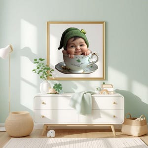 Könnte beinhalten: Ein gerahmter Druck mit einem Baby, das einen grünen Hut mit einem Kleeblatt trägt, in einer Teetasse. Die Tasse und Untertasse sind mit Kleeblättern und goldenen Verzierungen verziert. Das Bild hat ein St. Patrick's Day-Thema. Der Text auf der Tasse lautet "St. Patrick's Day 2023".