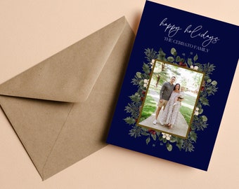 May include: A navy blue holiday card with the words "happy holidays" and "THE CERRATO FAMILY" in white script. The card features a family photo framed by a wreath of greenery and berries, with a brown envelope.