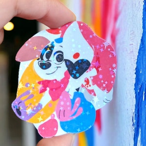 Puede incluir: Una pegatina colorida con un perro de dibujos animados que lleva un pañuelo rosa y un parche en el ojo azul. El perro está rodeado de un fondo blanco con estrellas rosas, azules y amarillas.